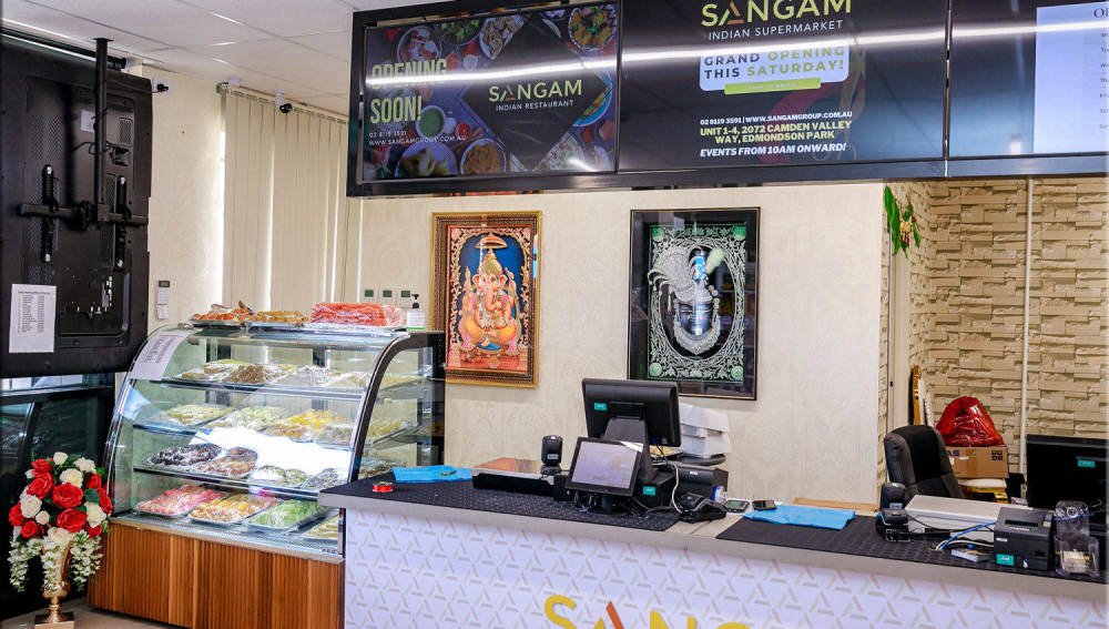 Framed Ganesha and Krishna artwork above the Sangam sweets counter