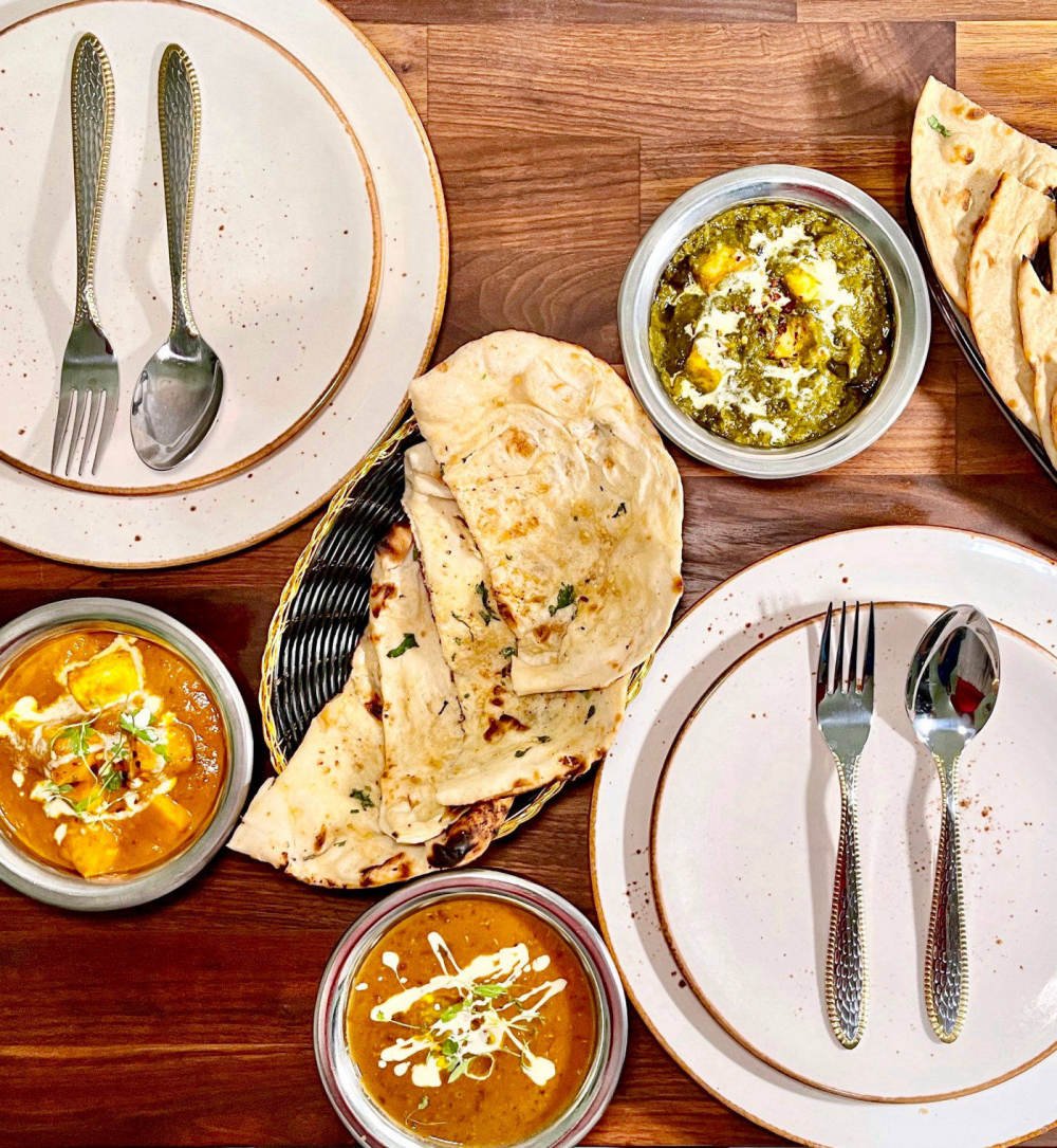 Sangam Indian Restaurant spread of garlic naan, paneer curries and dal on a wooden table